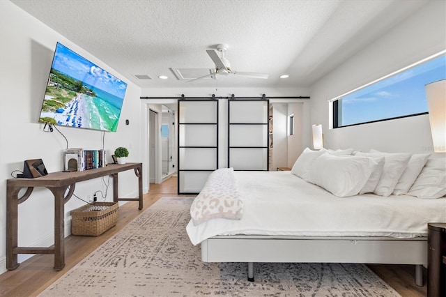 bedroom featuring a barn door, a textured ceiling, and light hardwood / wood-style floors