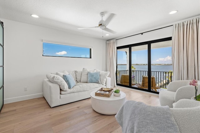 living room with ceiling fan, light hardwood / wood-style floors, a textured ceiling, and a water view