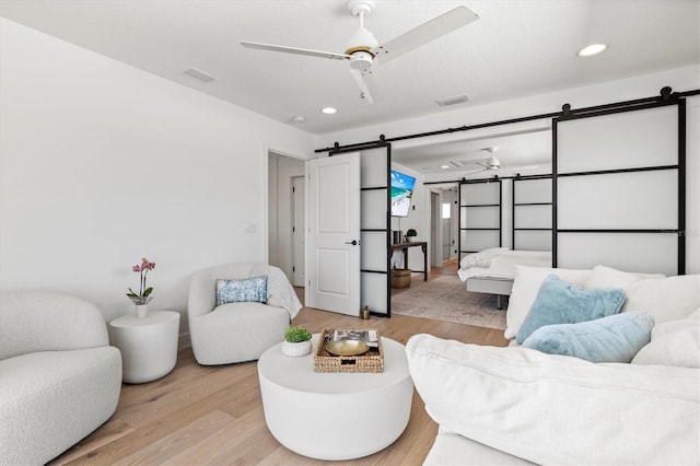 living room featuring ceiling fan, a barn door, and light hardwood / wood-style flooring