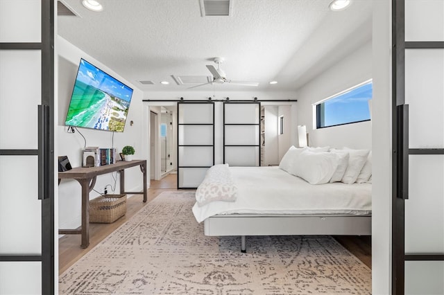 bedroom with a barn door, light hardwood / wood-style floors, and a textured ceiling