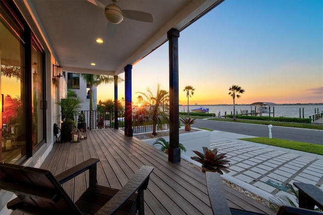 deck at dusk featuring a water view, ceiling fan, and covered porch