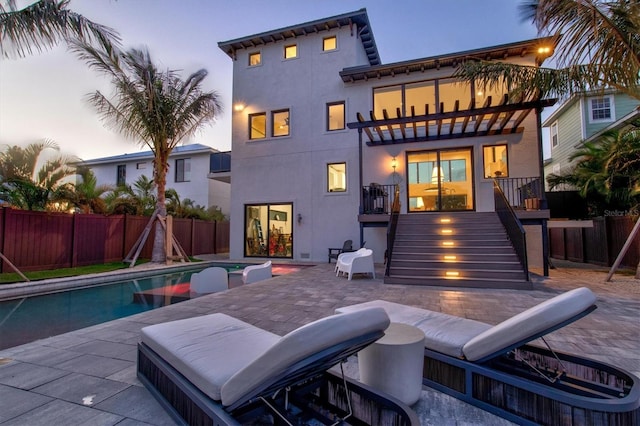 back house at dusk with a balcony, a fenced in pool, and a patio