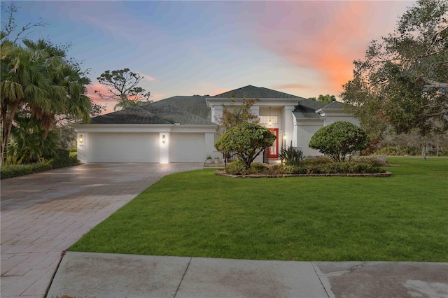 view of front of home featuring a yard, decorative driveway, an attached garage, and stucco siding