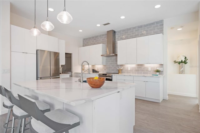 kitchen featuring decorative light fixtures, wall chimney range hood, stainless steel appliances, decorative backsplash, and white cabinets