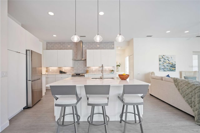 kitchen featuring appliances with stainless steel finishes, sink, white cabinets, hanging light fixtures, and wall chimney exhaust hood