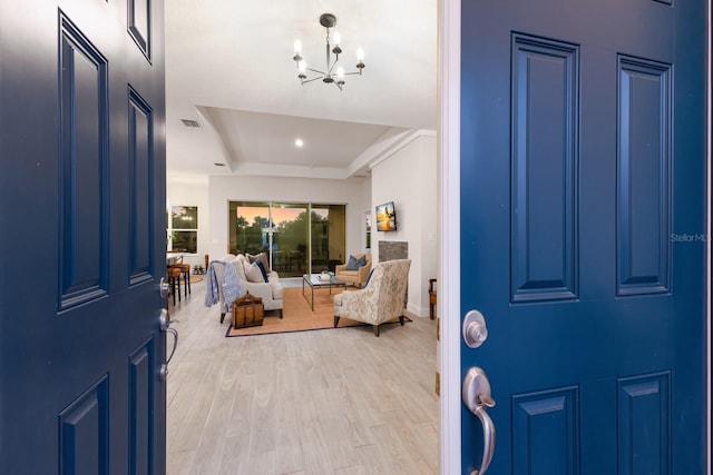 foyer featuring a raised ceiling, an inviting chandelier, and light wood-type flooring