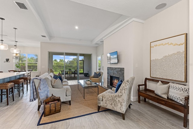 living room with a tray ceiling, a stone fireplace, and light hardwood / wood-style flooring