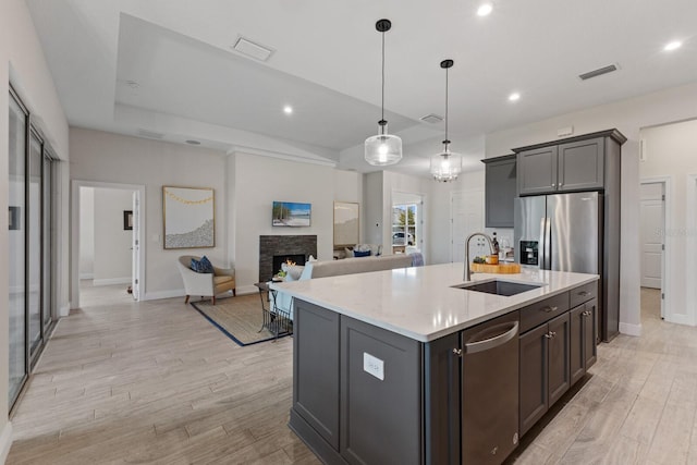 kitchen featuring light hardwood / wood-style floors, appliances with stainless steel finishes, a kitchen island with sink, hanging light fixtures, and sink