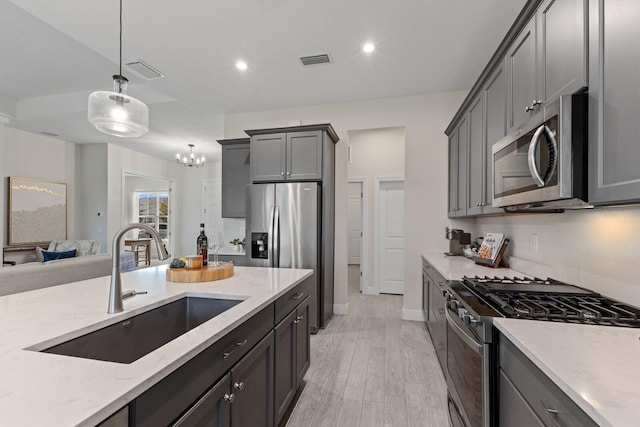 kitchen with pendant lighting, stainless steel appliances, light hardwood / wood-style floors, sink, and gray cabinetry