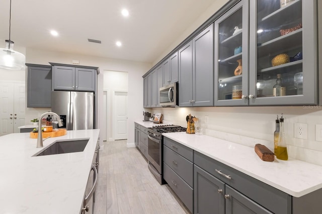 kitchen with light hardwood / wood-style floors, gray cabinets, stainless steel appliances, decorative light fixtures, and sink