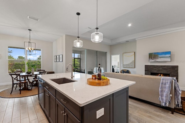 kitchen featuring decorative light fixtures, a kitchen island with sink, sink, and a stone fireplace