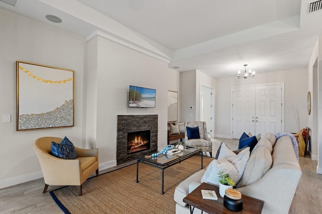 living room featuring light hardwood / wood-style flooring, a stone fireplace, and an inviting chandelier