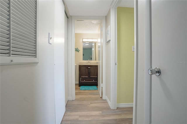 hall with light wood-type flooring, a textured ceiling, and sink