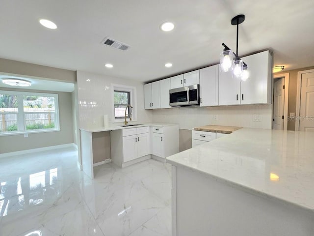 kitchen featuring pendant lighting, kitchen peninsula, sink, white cabinetry, and light stone countertops