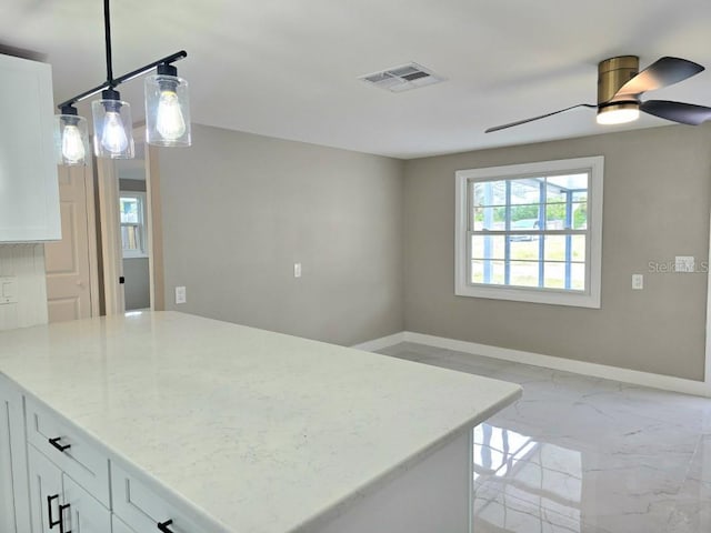 kitchen featuring hanging light fixtures, white cabinets, ceiling fan, and light stone countertops