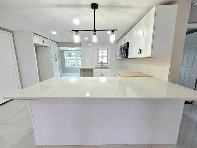 kitchen featuring kitchen peninsula, light stone countertops, white cabinetry, and pendant lighting