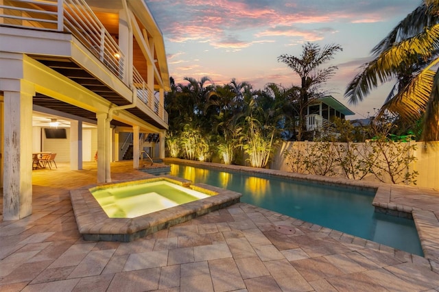 pool at dusk with an in ground hot tub and a patio