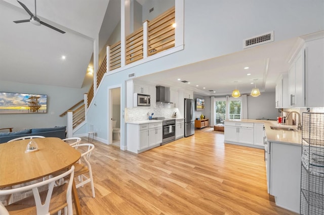 kitchen with appliances with stainless steel finishes, decorative backsplash, wall chimney exhaust hood, white cabinets, and sink