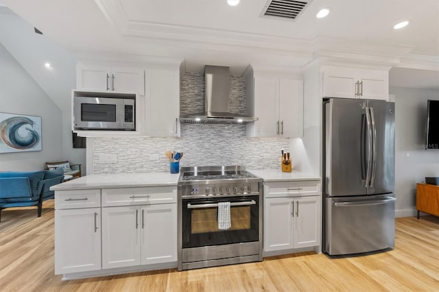 kitchen with stainless steel appliances, wall chimney exhaust hood, white cabinets, and tasteful backsplash