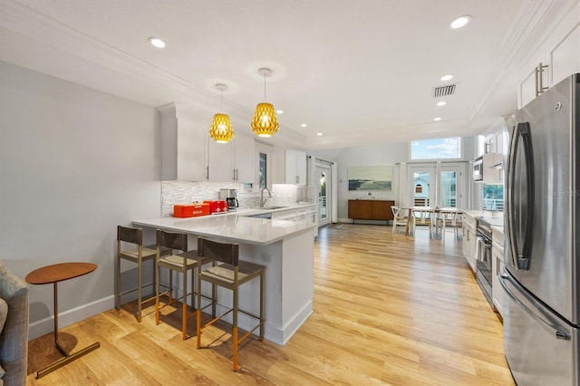 kitchen with kitchen peninsula, sink, white cabinetry, hanging light fixtures, and stainless steel appliances