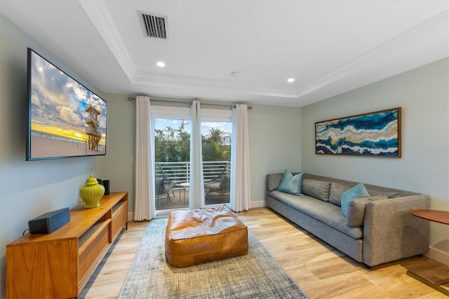 living room with light wood-type flooring, ornamental molding, and a raised ceiling