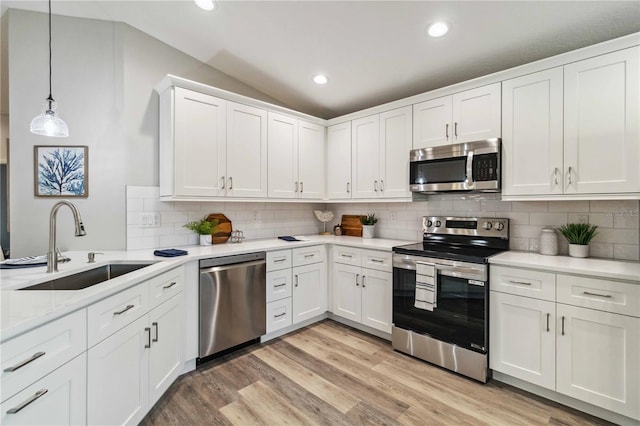 kitchen featuring white cabinetry, lofted ceiling, sink, hanging light fixtures, and stainless steel appliances