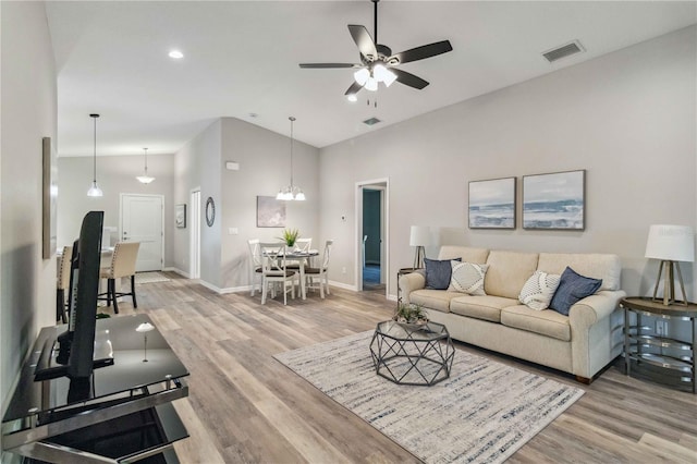 living room with ceiling fan with notable chandelier, light hardwood / wood-style flooring, and a high ceiling