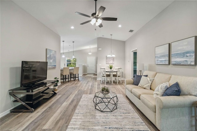 living room with ceiling fan with notable chandelier, lofted ceiling, and hardwood / wood-style floors