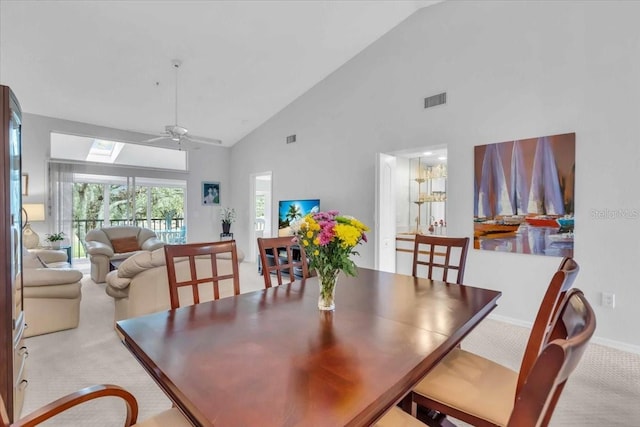 dining room featuring ceiling fan, light colored carpet, high vaulted ceiling, and a skylight