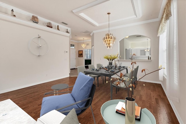 dining space featuring ornamental molding, dark wood-type flooring, a notable chandelier, and a raised ceiling