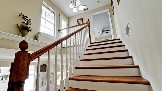 staircase featuring ceiling fan with notable chandelier and a towering ceiling