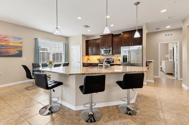 kitchen featuring light stone counters, appliances with stainless steel finishes, a kitchen bar, and a center island with sink