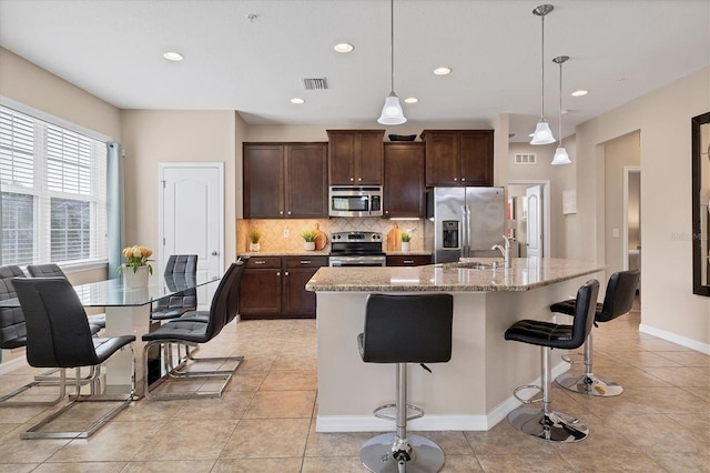 kitchen with a kitchen island with sink, stainless steel appliances, decorative backsplash, a kitchen bar, and decorative light fixtures