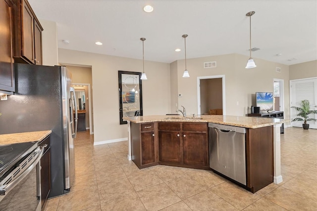 kitchen featuring sink, decorative light fixtures, appliances with stainless steel finishes, an island with sink, and light stone countertops