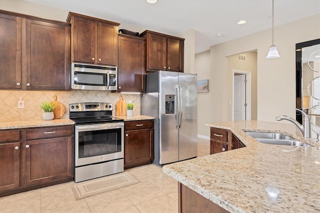 kitchen featuring sink, light stone counters, hanging light fixtures, stainless steel appliances, and backsplash