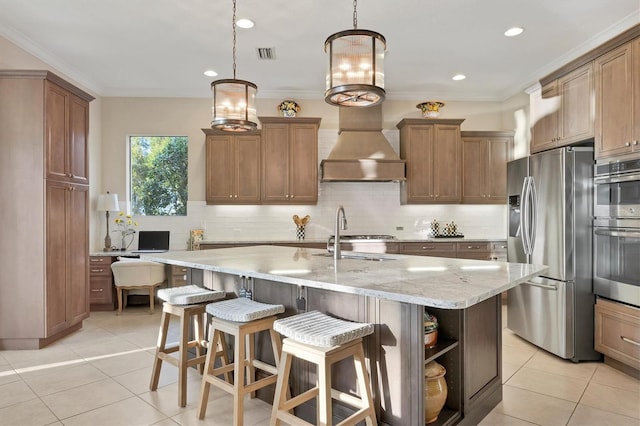 kitchen with pendant lighting, appliances with stainless steel finishes, sink, light stone countertops, and an island with sink