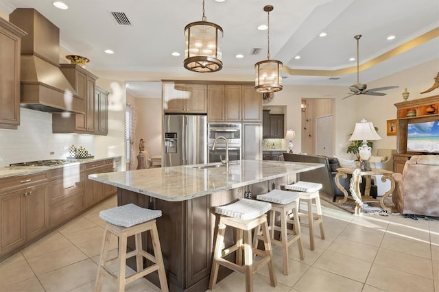 kitchen featuring a spacious island, appliances with stainless steel finishes, custom exhaust hood, a raised ceiling, and a breakfast bar