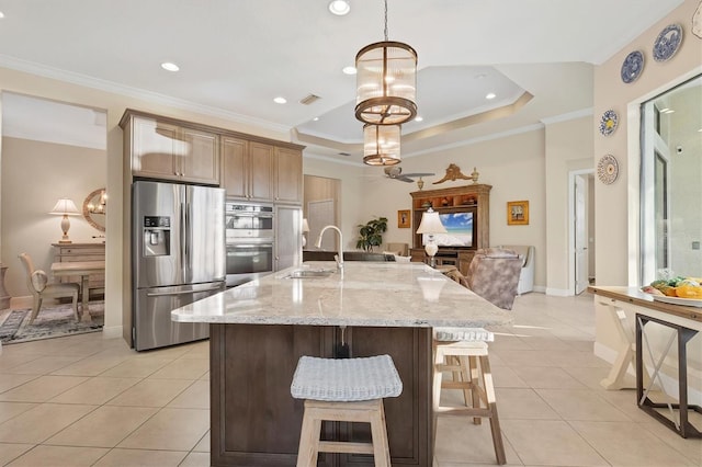 kitchen with pendant lighting, appliances with stainless steel finishes, sink, a tray ceiling, and a large island with sink