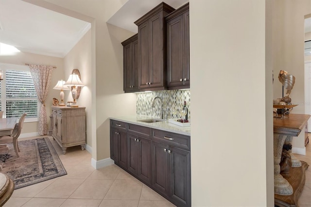 bar with dark brown cabinets, sink, light stone counters, light tile patterned flooring, and decorative backsplash