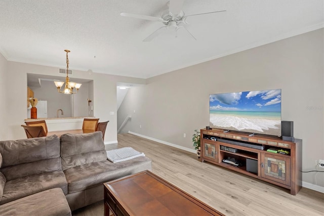 living room with ceiling fan with notable chandelier, a textured ceiling, ornamental molding, and light wood-type flooring