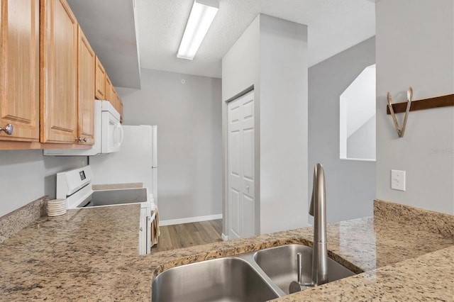 kitchen featuring a textured ceiling, sink, light stone counters, and white appliances