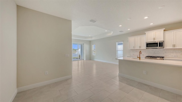 kitchen with a raised ceiling, backsplash, stove, light tile patterned flooring, and white cabinets