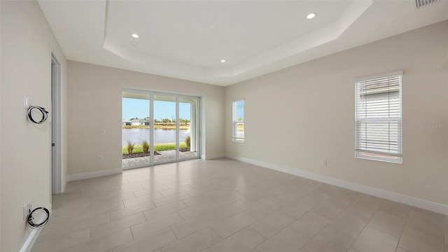 empty room featuring a water view, light tile patterned floors, and a tray ceiling