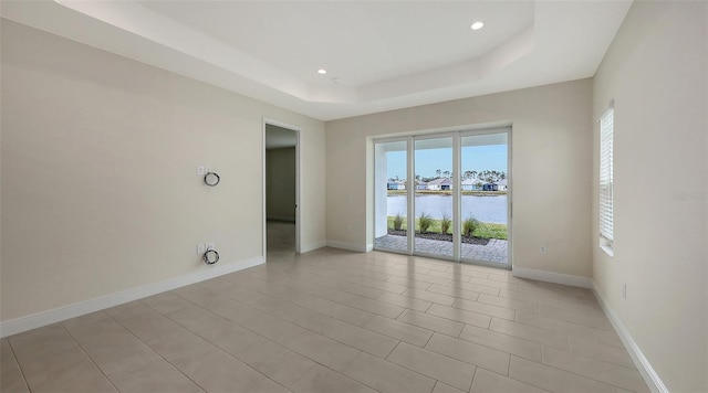 spare room with light tile patterned floors, a tray ceiling, and a water view