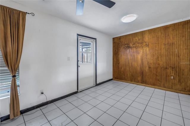 empty room featuring ceiling fan, light tile patterned floors, and wood walls