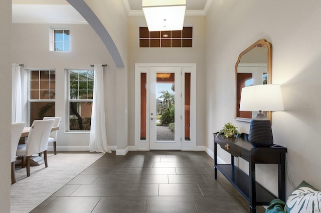 entrance foyer featuring dark tile patterned flooring, crown molding, a towering ceiling, and baseboards