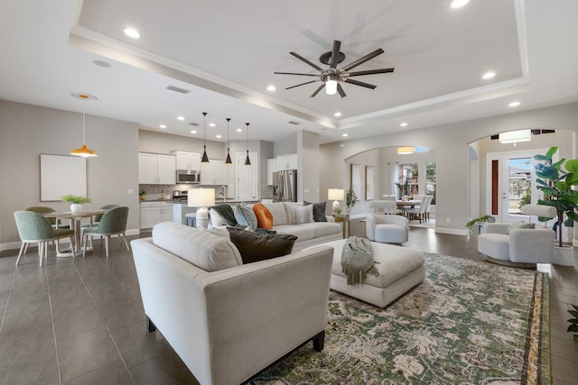 living room featuring ornamental molding, a tray ceiling, visible vents, and arched walkways