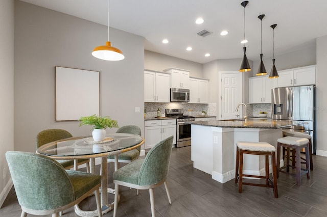 kitchen featuring a sink, visible vents, appliances with stainless steel finishes, backsplash, and a center island with sink