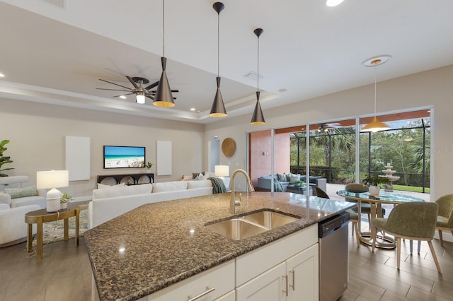 kitchen with pendant lighting, sink, a raised ceiling, white cabinets, and dark stone counters