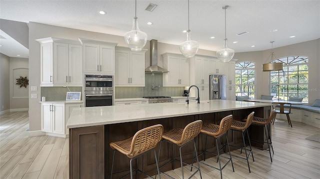 kitchen featuring a large island, decorative light fixtures, and wall chimney range hood